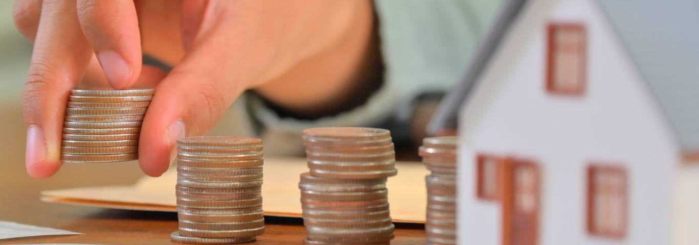 ręka układa stosy monet obok modelu domu i dokumentów