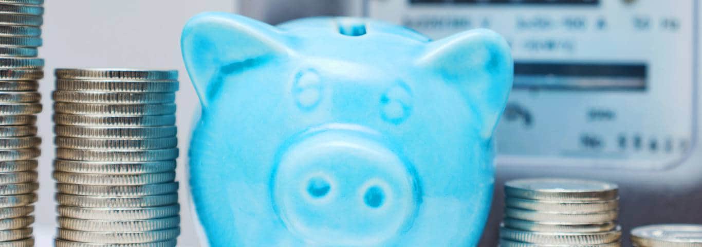 Oszczędności na energii – świnka skarbonka z monetami i licznik prądu symbolizujące dopłaty do rachunków