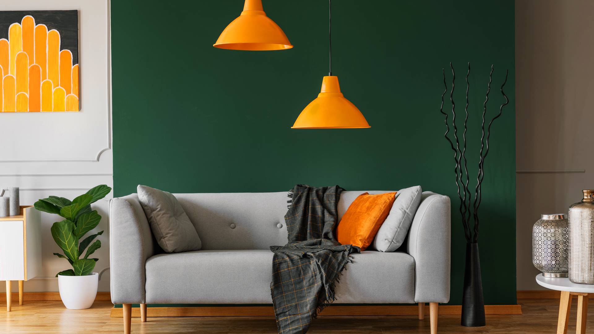 szara sofa z poduszkami i pomarańczowymi lampami na tle zielonej ściany
