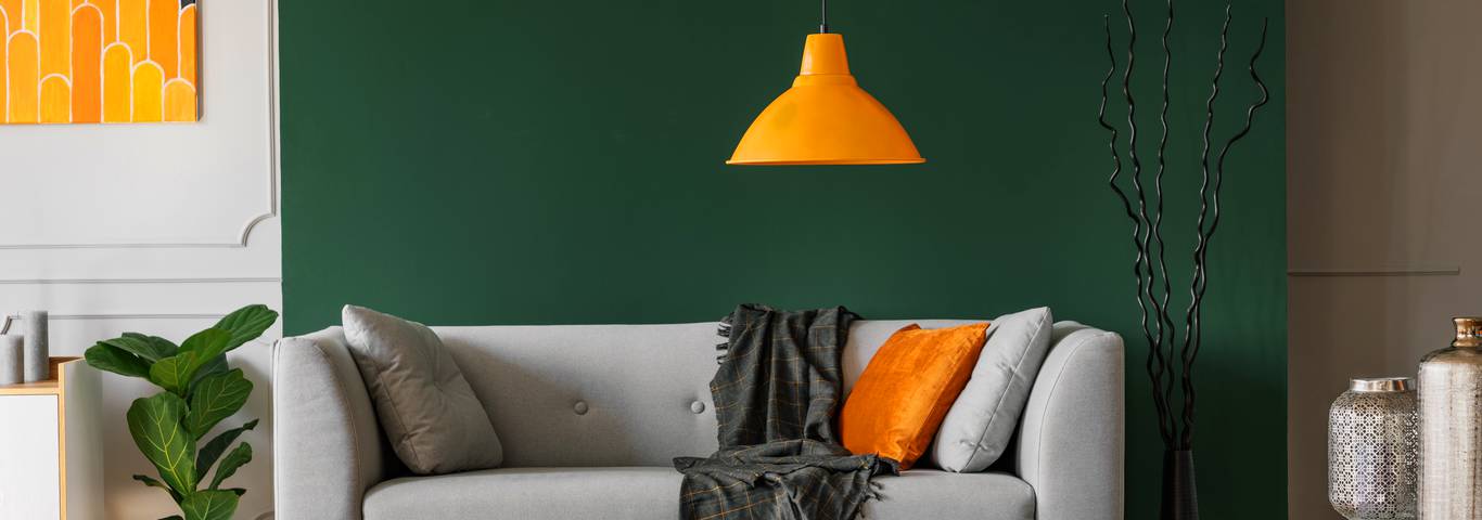 szara sofa z poduszkami i pomarańczowymi lampami na tle zielonej ściany
