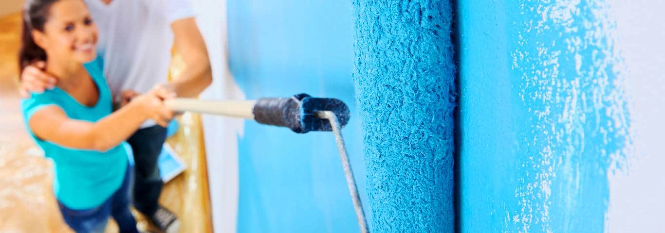 zbliżenie na wałek malarski trzymany przez uśmiechniętą kobietę