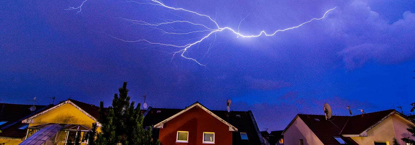 Błyskawica nad domem jednorodzinnym podczas burzy – przykład zagrożenia, przed którym chroni uziemienie