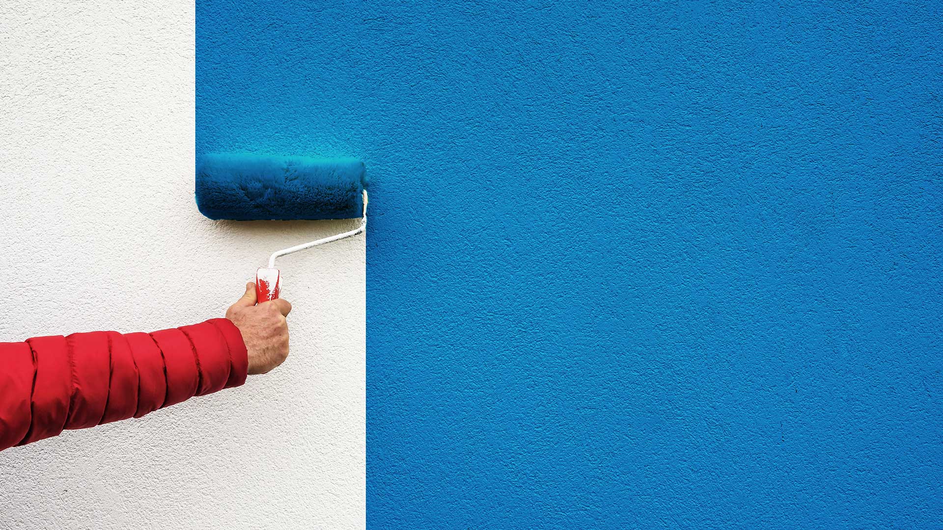 mężczyzna maluje ścianę wałkiem na niebiesko