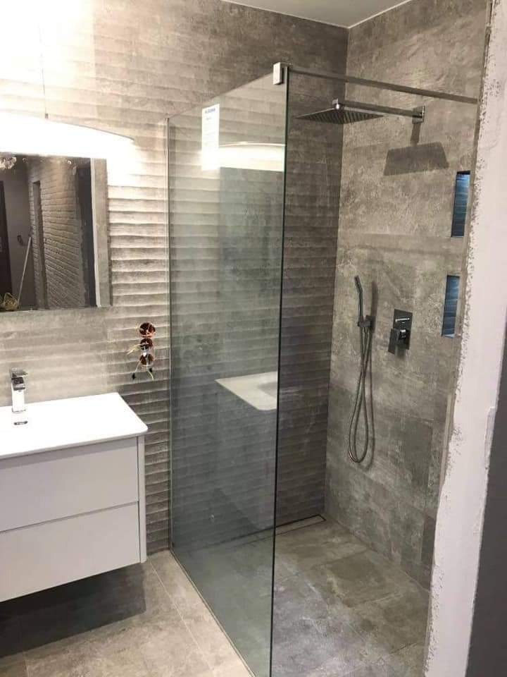 Nowoczesna łazienka z szarą, teksturowaną glazurą, kabiną prysznicową typu walk-in z deszczownicą, białą szafką pod umywalką i minimalistyczną armaturą.