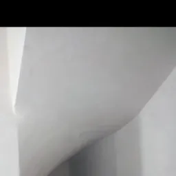 Gładka, biała powierzchnia ściany i sufitu po tynkowaniu, z widocznymi zaokrągleniami i delikatnymi przejściami światłocieni.