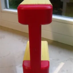 Czerwono-żółty dźwigar szalunkowy H20, okuty, sfotografowany na blacie, z oknem w tle.