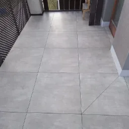 Wykończony balkon z szarą, kwadratową posadzką z płytek i czarną metalową balustradą, widoczny fragment drabiny malarskiej.