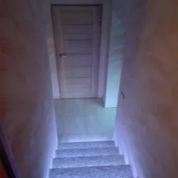 Kamienne schody z podświetleniem LED prowadzące do pomieszczenia z tynkiem dekoracyjnym Trawertyn i drewnianymi drzwiami.