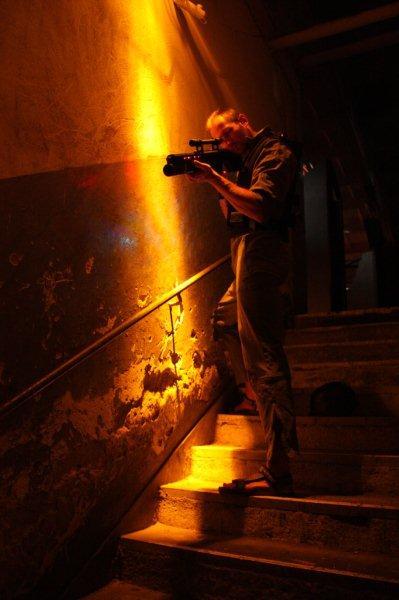 Mężczyzna celuje z karabinu laserowego stojąc na schodach w pomieszczeniu oświetlonym pomarańczowym światłem, przygotowany do laserowego paintballa.