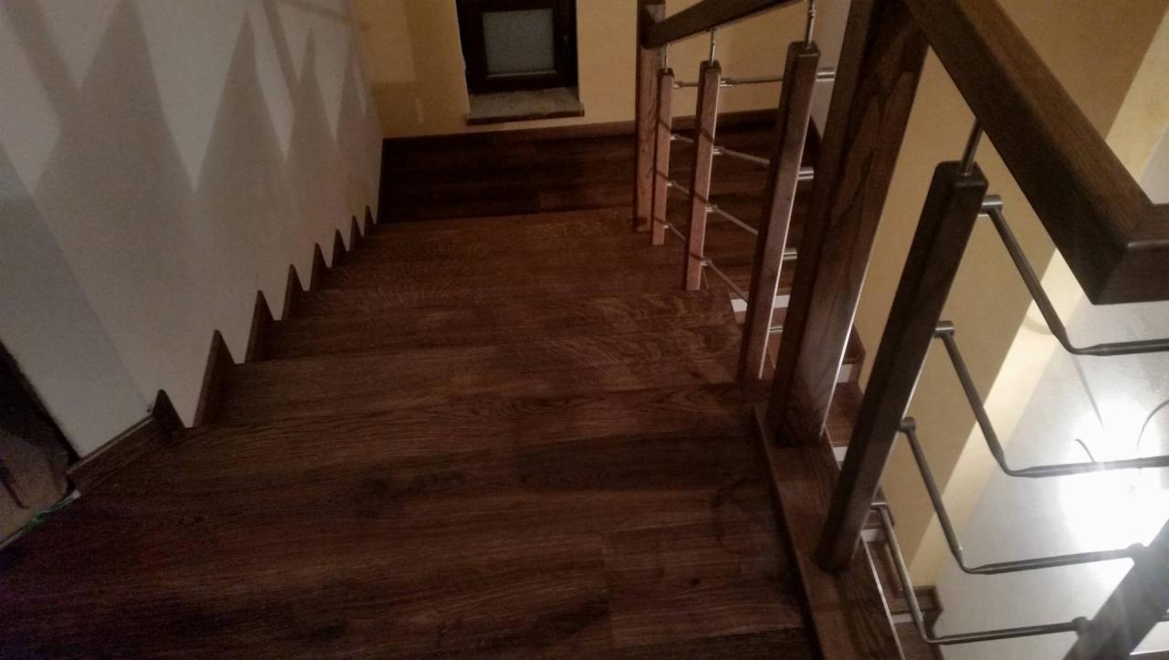 Schody drewniane z ciemnego drewna z metalową balustradą, widok z góry na dół, oświetlenie mieszane.