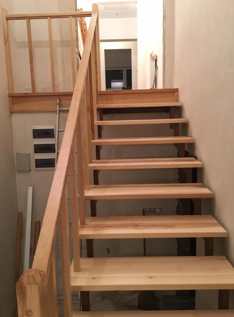 Surowe drewniane schody z balustradą w trakcie montażu, widoczne elementy konstrukcyjne i drabina oparta o ścianę.