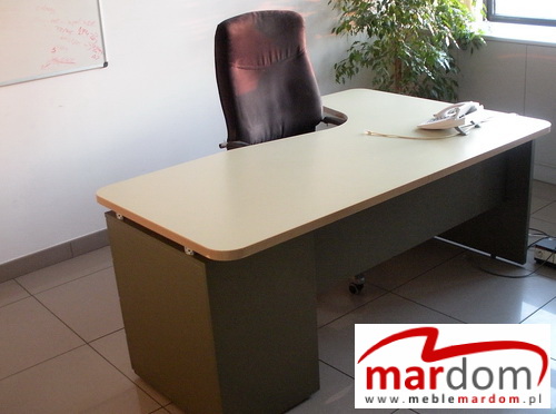 Beżowo-szare biurko biurowe z krzesłem na kółkach i telefonem stacjonarnym, widok z boku, w tle roślina doniczkowa.