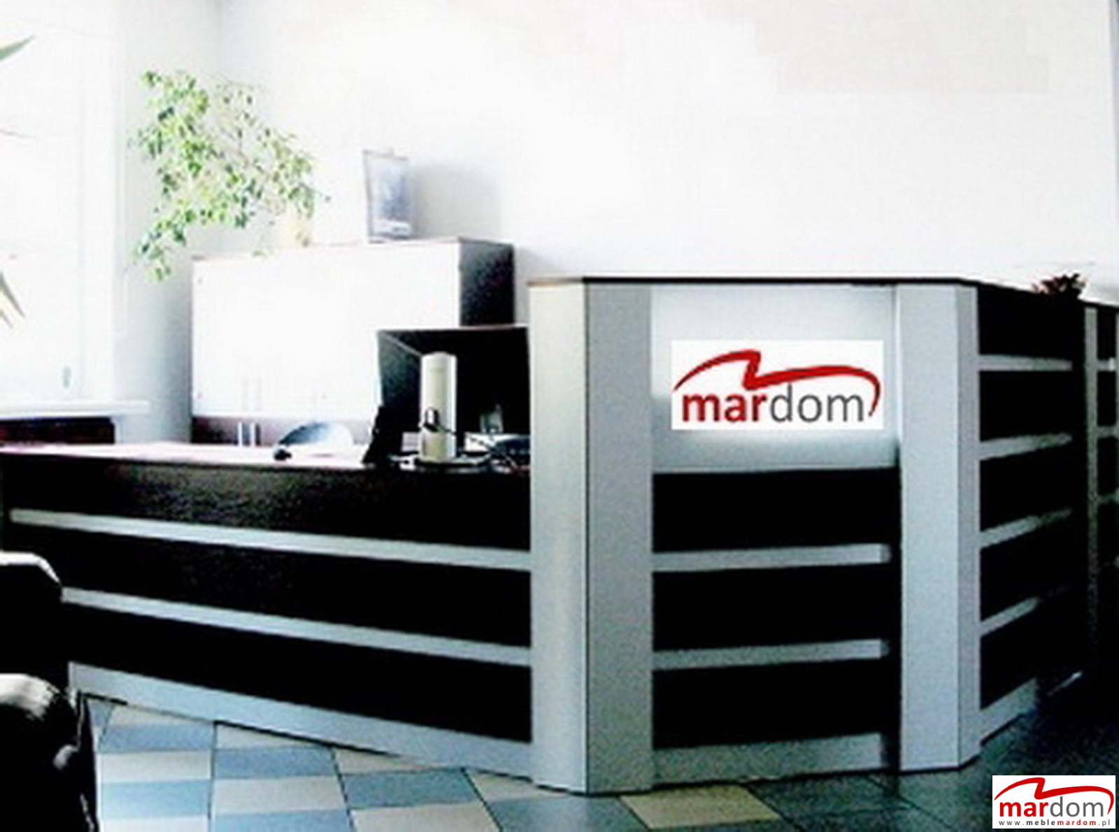 Recepcja biurowa z logo firmy mardom.pl, widoczne biurko, monitor i roślina doniczkowa, oświetlenie dzienne