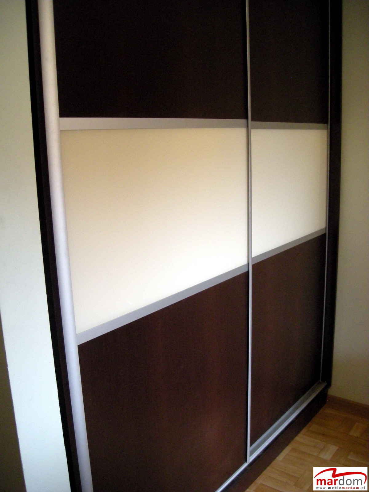 Dwukolorowa szafa przesuwna z ciemnobrązowymi i kremowymi panelami, widoczne prowadnice i podłoga z paneli.