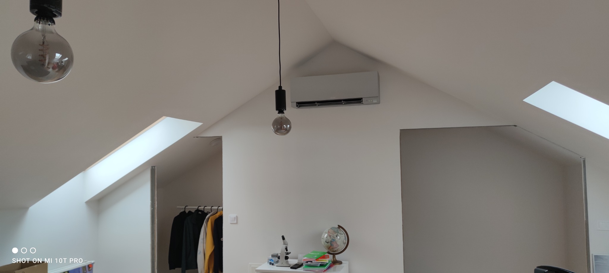 Zamontowana jednostka klimatyzacji na poddaszu w pokoju z oknami dachowymi, widoczne oświetlenie i wyposażenie pokoju.