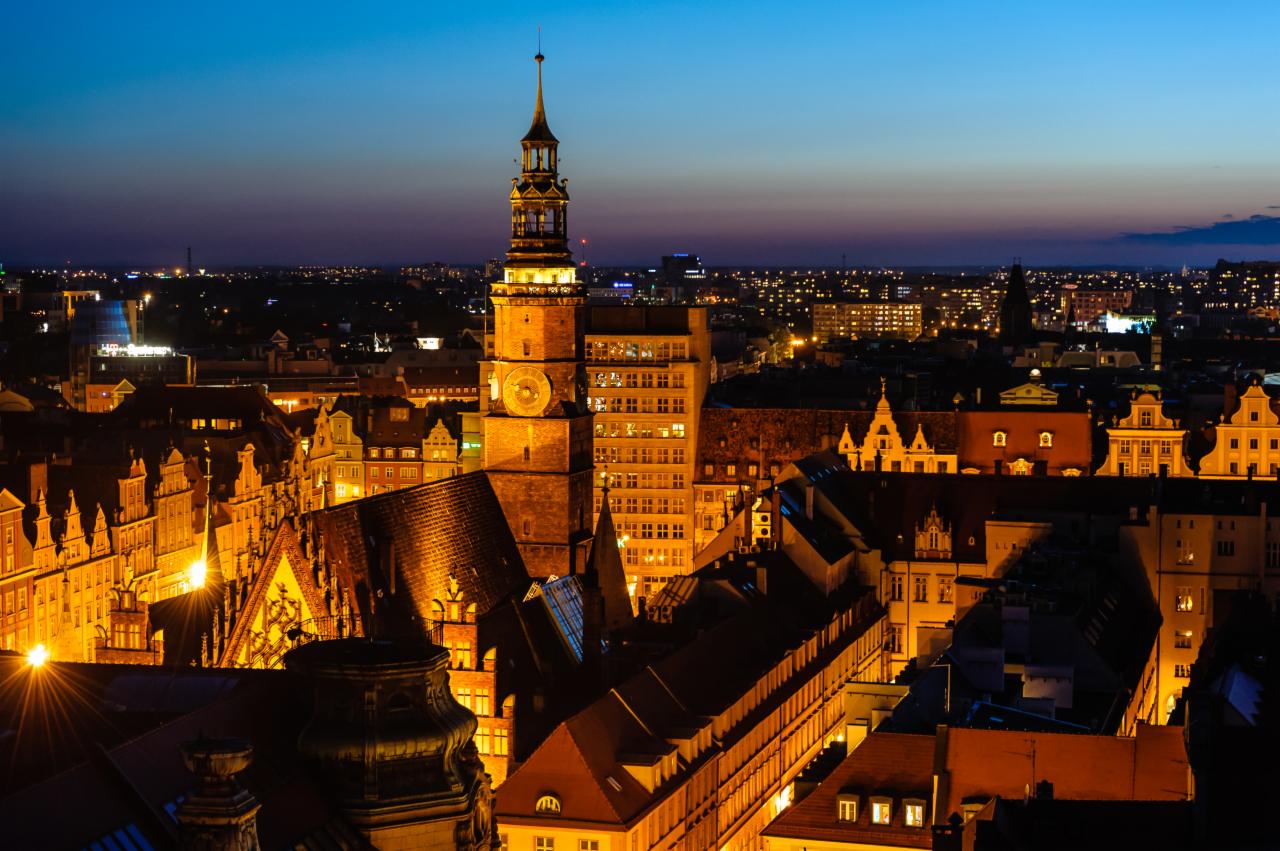 Nocna panorama Wrocławia z widokiem na oświetlony Ratusz i Stare Miasto, z delikatną poświatą w tle.