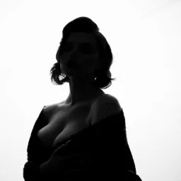 Czarno-biała sylwetka kobiety z tatuażem 'Angel' na ramieniu, stylizowana fryzura, ujęcie od dołu.