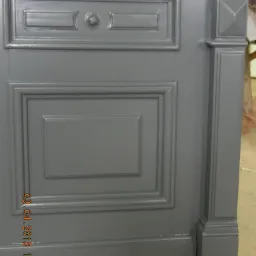 Odnowione, szare drzwi z dekoracyjnymi panelami i listwami, ukazujące precyzję renowacji i dbałość o detale architektoniczne. Częściowy widok.