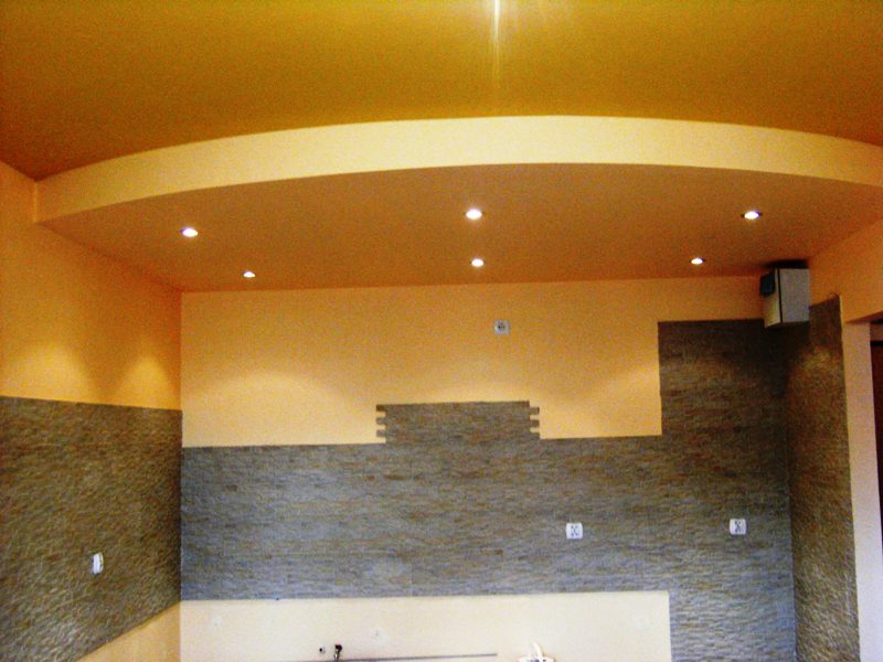 Żółto-pomarańczowe wnętrze z częściowo wykończoną ścianą z kamienia dekoracyjnego i podwieszanym sufitem z oświetleniem punktowym.