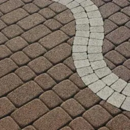 Ułożona nawierzchnia z prostokątnej, brązowej kostki brukowej z p&oacute;łkolistym wzorem z szarej kostki. Widok z g&oacute;ry.