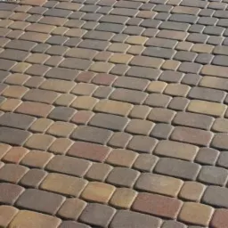 Ułożona nawierzchnia z prostokątnej kostki w odcieniach brązu, beżu i szarości, wzór parkietowy, widok z góry.