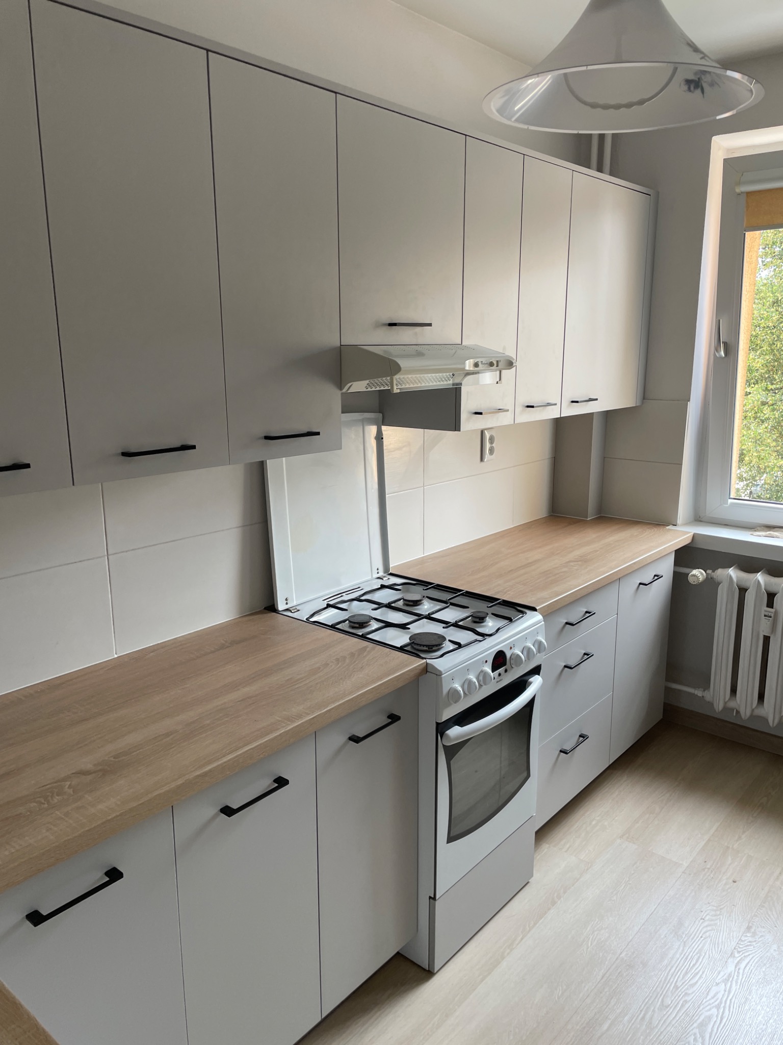 Jasna kuchnia na wymiar z drewnianym blatem, czarnymi uchwytami i białą kuchenką gazową pod okapem.