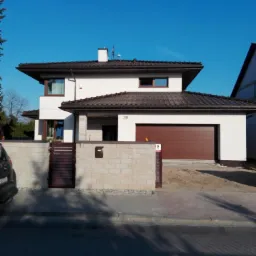 Dwukondygnacyjny dom z brązowym dachem, garażem i ogrodzeniem z jasnych bloczków, widoczny numer domu '36' oraz boczna furtka z drewnianymi schodami.