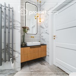 DD Projekt - Nowoczesna łazienka z marmurowymi płytkami, wiszącą szafką z umywalką nablatową, grzejnikiem drabinkowym i złotymi akcentami.