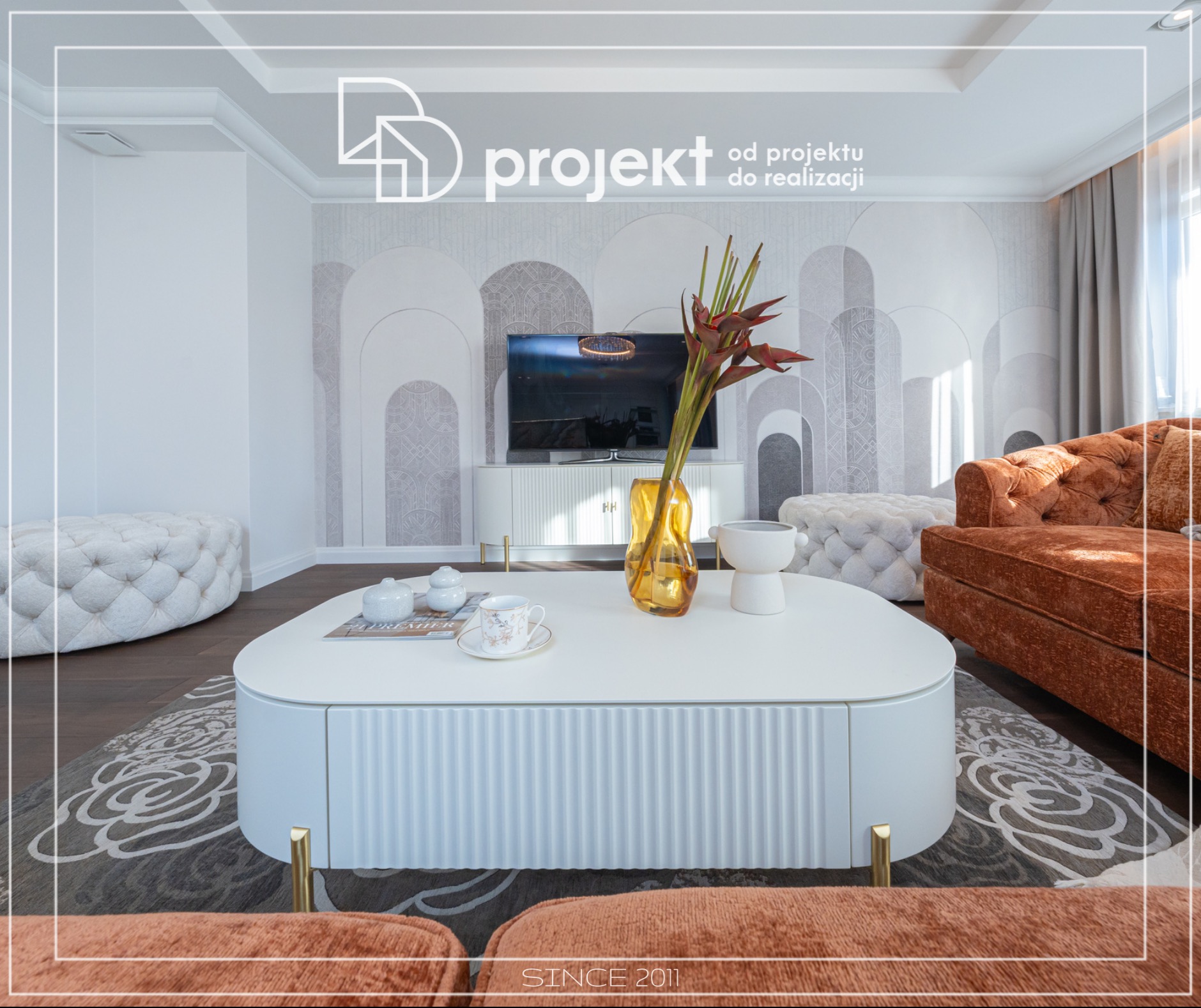 Jasne wnętrze salonu w stylu art deco z tapetą w geometryczne wzory, biały stolik kawowy z dekoracjami, pomarańczowa sofa i pufy z pikowaniem.