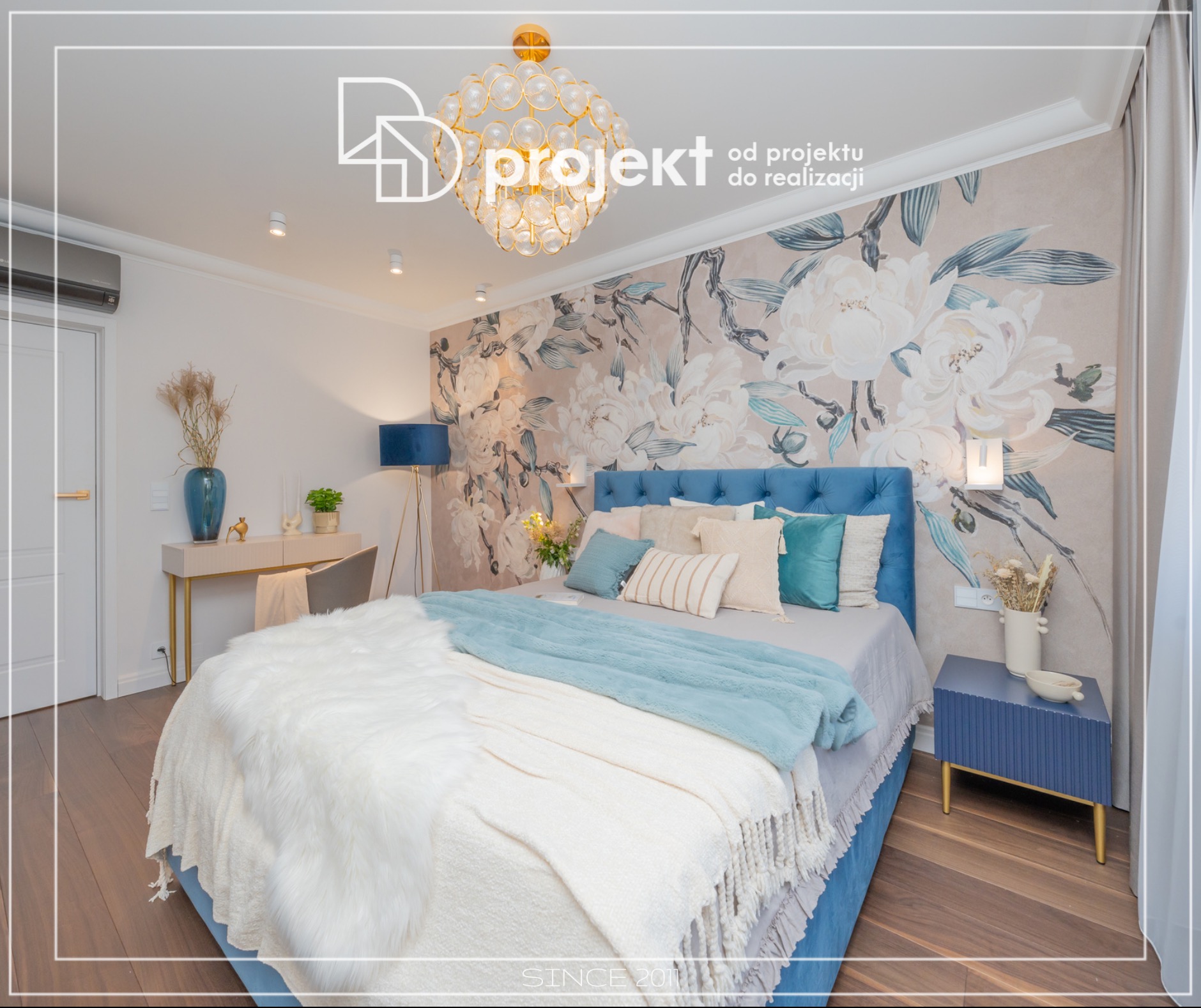 Elegancka sypialnia z niebieskim łóżkiem, tapetą w kwiaty i designerską lampą, oświetlona przez boczne lampki nocne i lampę podłogową, z dekoracyjnym biurkiem i dodatkami w odcieniach beżu i złota.