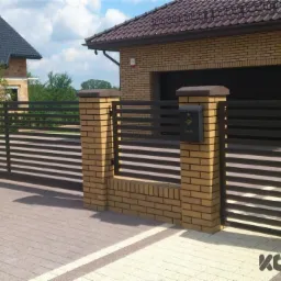 Nowoczesna brama wjazdowa przesuwna z poziomymi, metalowymi szczeblami, osadzona na ceglanych słupkach z szarymi daszkami, z widocznym domem jednorodzinnym w tle.