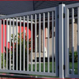 Szare ogrodzenie palisadowe z pionowych profili stalowych, widoczne na tle czerwonego domu z białymi obramowaniami okien i ciemnym dachem, z zielonymi krzewami przed ogrodzeniem.