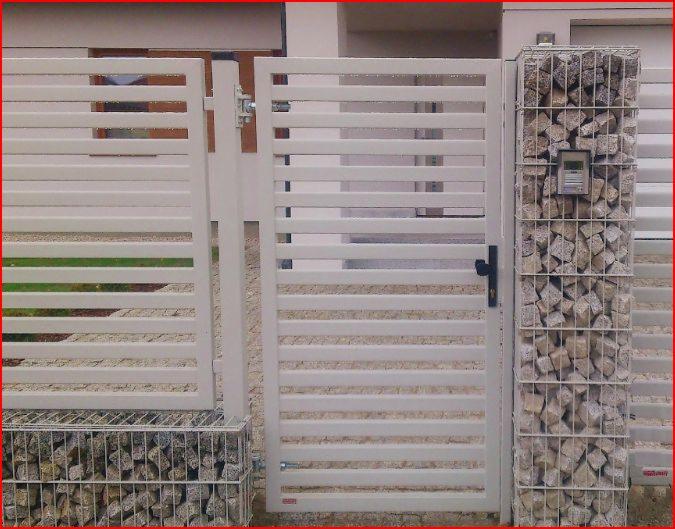 Nowoczesna brama wjazdowa z poziomymi przęsłami w kolorze jasnego beżu, osadzona na gabionowych podstawach i słupku, z domofonem na słupku.