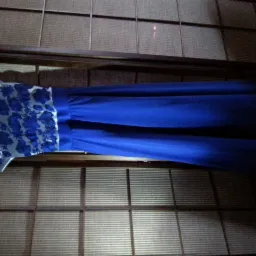 Kobaltowa suknia wieczorowa z koronkową górą, zawieszona na różowym wieszaku na tle ściany w stylu japońskim. Delikatne światło podkreśla detale sukni.