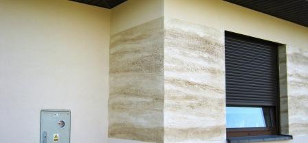 Elewacja zewnętrzna budynku z dekoracyjnym tynkiem imitującym naturalny kamień, okno z roletą zewnętrzną, skrzynka elektryczna na ścianie.