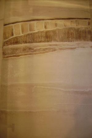 Beżowa ściana z dekoracyjnym tynkiem imitującym krajobraz z geometrycznymi elementami, widoczne pionowe i poziome struktury.