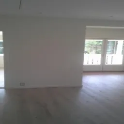 Jasne, puste wnętrze po remoncie. Parkiet z naturalnego drewna, świeżo pomalowane białe ściany, okno z widokiem na zieleń. Minimalistyczny design.