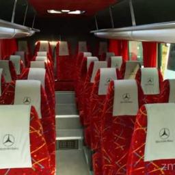 Trans Rd - Wnętrze autobusu z czerwonymi siedzeniami z białymi zagłówkami z logo Mercedes-Benz, widok z przodu, czerwone zasłony i szare schodki na środku przejścia.
