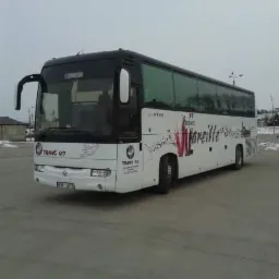 Biały autokar z czarnym dachem, z logo firmy Trans RD na boku, zaparkowany na betonowym placu w pochmurny dzień.