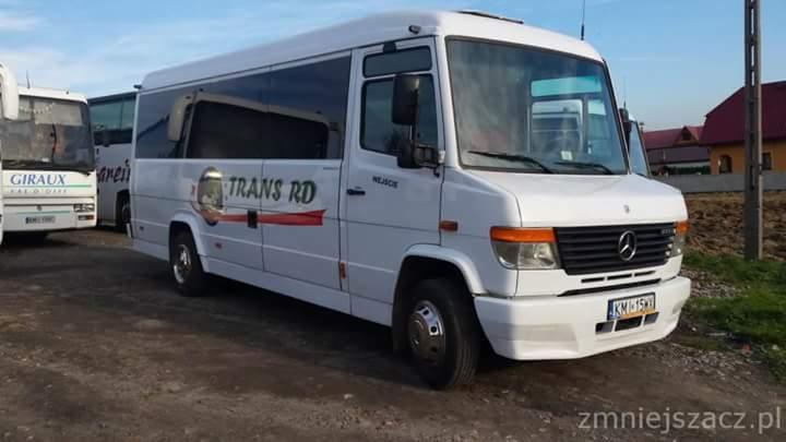 Biały Mercedes-Benz bus z logo 'TRANS RD' na boku, zaparkowany na żwirowym podłożu, z widocznymi innymi autobusami w tle.