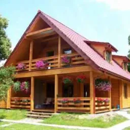 Dwukondygnacyjny dom z drewna z czerwonym dachem, balkonem i werandą, ozdobiony wiszącymi donicami z kwiatami.