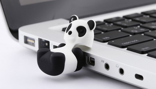 Pendrive w kształcie pandy podłączony do portu USB laptopa, widoczne czarne klawisze laptopa i białe tło.