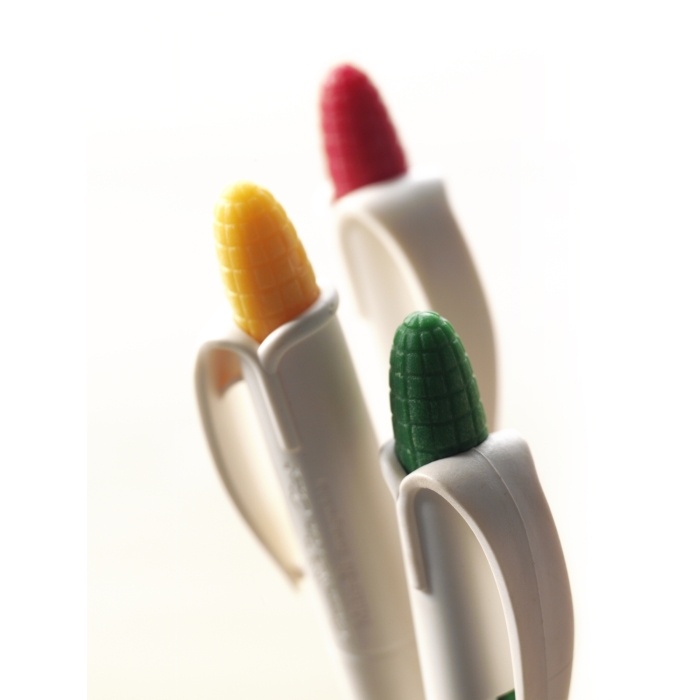 Trzy długopisy w kształcie kolb kukurydzy w kolorach: żółtym, zielonym i czerwonym, umieszczone na białym tle.