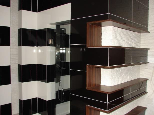 Nowoczesna łazienka z czarno-białymi płytkami ułożonymi w pasy, szklana kabina prysznicowa z chromowaną armaturą i półki z ciemnego drewna z białymi dekoracyjnymi elementami.