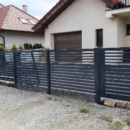 Nowoczesne, poziome ogrodzenie panelowe i furtka w kolorze grafitowym, z widocznym domofonem przy wejściu, na tle domu z numerem 2.
