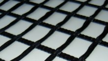Czarna geosiatka o romboidalnych oczkach ułożona na białym tle, sfotografowana z bliska pod kątem.