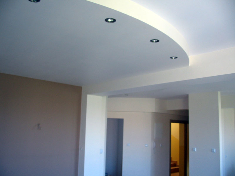 Wnętrze z wykończoną, podwieszaną, łukowatą częścią sufitu z wbudowanymi punktowymi oprawami oświetleniowymi, kremowe ściany i widoczne wejście do innego pomieszczenia.