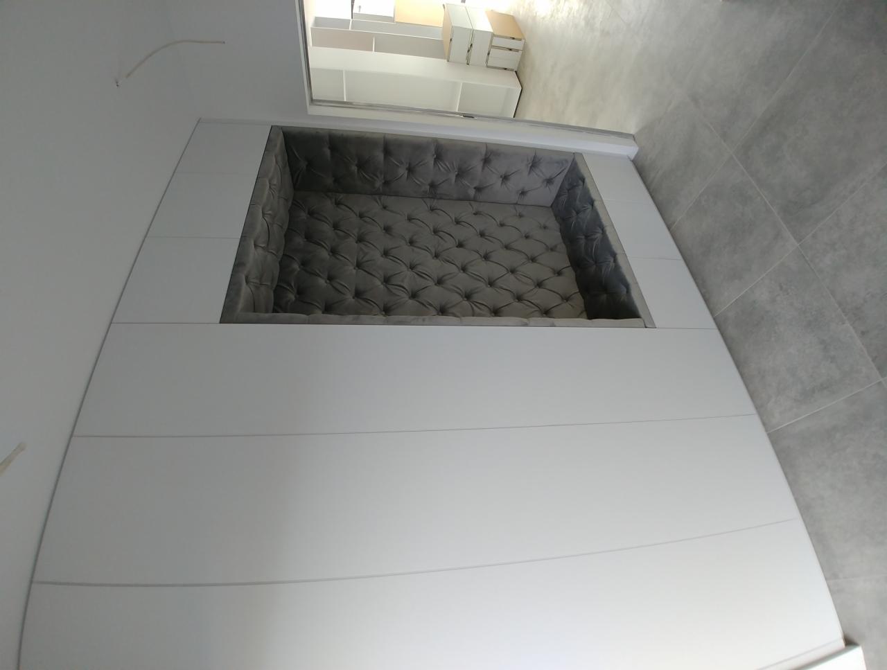 Wnęka z tapicerowanym siedziskiem w zabudowie meblowej z białymi frontami, widok z góry, szare płytki podłogowe.