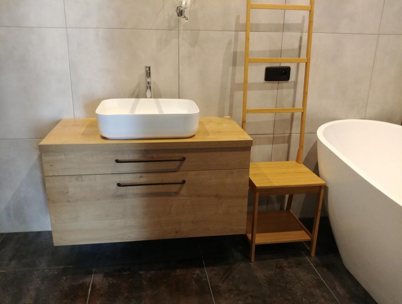 Łazienka z drewnianą szafką pod umywalkę nablatową, drabinką na ręczniki i wolnostojącą wanną.