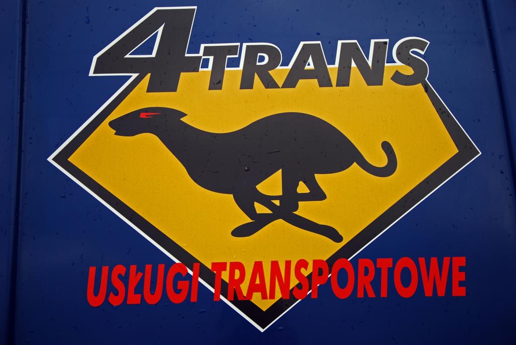Logo firmy transportowej 4Trans z sylwetką biegnącego charta na żółtym tle w kształcie rombu, umieszczone na niebieskim pojeździe.